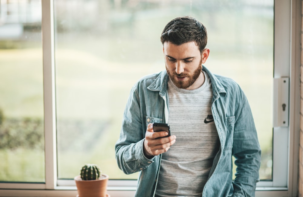 Homme regardant son téléphone près d'une fenêtre, illustration de la charge mentale anticipatoire liée à l'actualité internationale